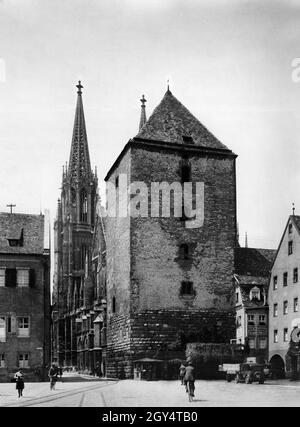 "Der Blick geht von Osten auf den Römerturm an der Domstraße in der Regensburger Altstadt. Zwei Radfahrer überqueren den Platz ''Alter Kornmarkt''. Links ist ein Teil des Herzoggerichts zu sehen. Im Eckhaus rechts befindet sich eine 'Wagenbau-Anstalt und mechanische Werkstätte'. Das undatierte Foto wurde wahrscheinlich in den 1930er Jahren aufgenommen. [Automatisierte Übersetzung]' Stockfoto