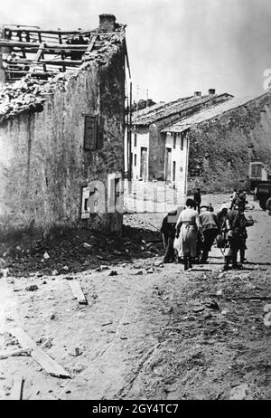 Eine kleine Gruppe französischer Flüchtlinge durchläuft eine Stadt, deren Häuser durch Bombenangriffe zerstört wurden. [Automatisierte Übersetzung] Stockfoto