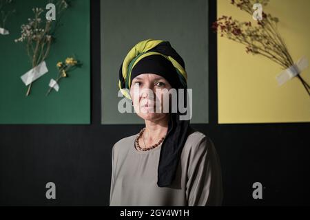 Porträt einer reifen muslimischen Frau in einem Hijab, die die Kamera an der Designwand ansieht Stockfoto
