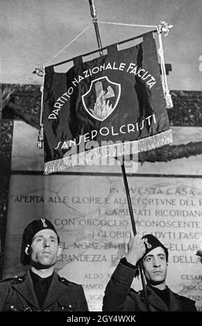 „ein Standardträger hält 1939 die 1. Sturmflagge der Partito Nazionale Fascista. Er steht vor einer Gedenktafel für die ''heroisch gefallenen Faschisten''. Auf der Flagge steht: ''Partito Nazionale Fascista / Sansepolcristi'', in der Mitte das Symbol der Faschisten, die Faschisten, die in einem Feuer brennen. [Automatisierte Übersetzung]' Stockfoto