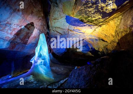 Lichtshow über Eisformationen und eine hohe Eisspitze im Parzivaldom an der Dachstein Rieseneishöhle, einer riesigen Eishöhle in den österreichischen Alpen Stockfoto