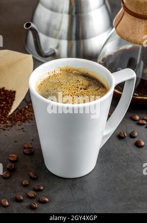 Eine Tasse Kaffee und die dritte Generation gießen über die Kaffeemaschine auf dem Steinboden Stockfoto