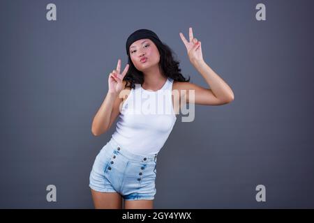 Junge chinesische Mädchen mit Bandana und Shorts, die den Frieden oder Sieg Zeichen, in einer lustigen Pose und Ausdruck. Stockfoto