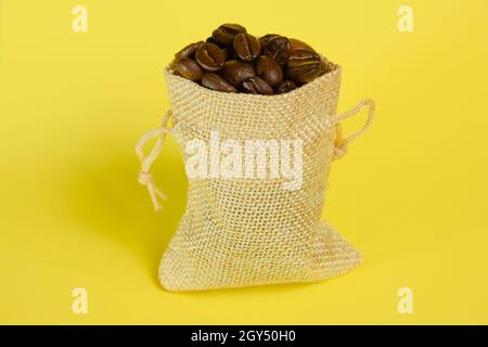 Kleine dekorative Tasche aus Hanf-leichtem Stoff mit Kaffeebohnen auf hellgelbem Hintergrund in Nahaufnahme Stockfoto