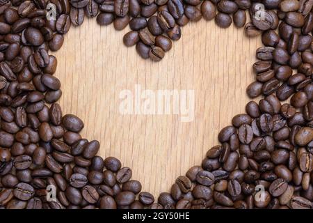 Ein Herz ist auf einer Holzfläche aus Kaffeebohnen angelegt. In der Mitte befindet sich eine Leere in Form eines Herzens für eine Inschrift. Stockfoto