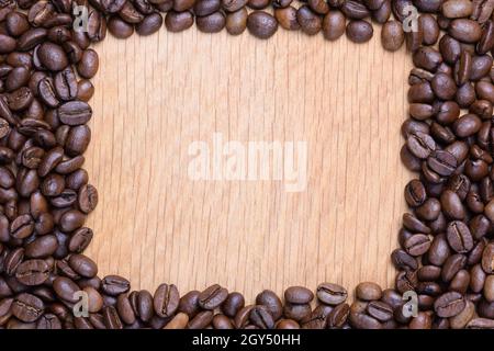 Auf einer braunen Holzoberfläche aus Kaffeebohnen wird eine rechteckige Leere angelegt. In der Leere ist Platz für eine Inschrift. Stockfoto