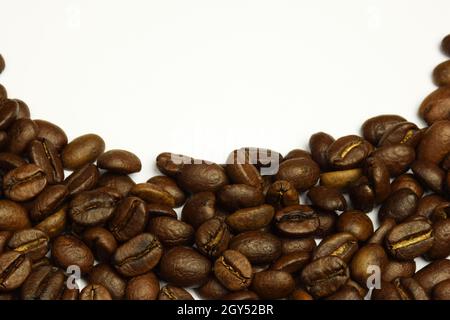 Geröstete Kaffeesorten, die in einem Halbkreis auf weißem Hintergrund verstreut sind. Die Oberseite des Fotos ist leer für eine Inschrift. Nahaufnahme fotografiert. Stockfoto