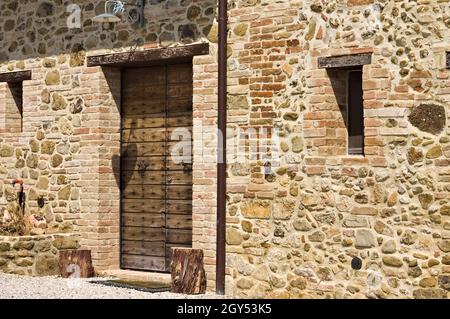 Eine Fassade eines alten Bauernhaus aus Stein mit einer Holztür und zwei kleinen Fenstern in der italienischen Landschaft (Toskana, Italien, Europa) Stockfoto