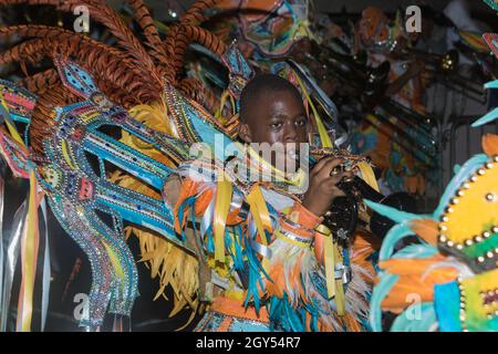 Junger Mann, Junge, bläst eine Trompete, während er in einem farbenfrohen Kostüm für die Junkanoo Straßenparade gekleidet ist Stockfoto