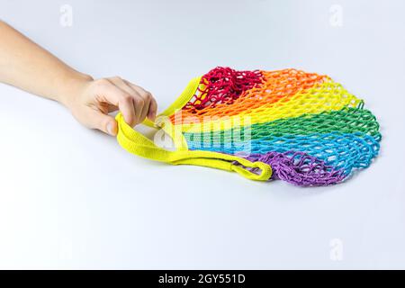 Eine Frauenhand hält eine wiederverwendbare Einkaufstasche aus Baumwolle, bunte Regenbogen-LGBT-Trendfarben. Auf einem hellgrauen Hintergrund. Das Konzept der Zero Waste, Stockfoto