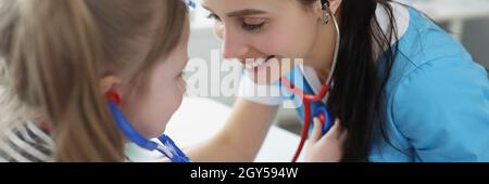 Arzt hört dem kleinen Mädchen mit Stethoskop zu und spielt mit ihr in der Klinik Stockfoto