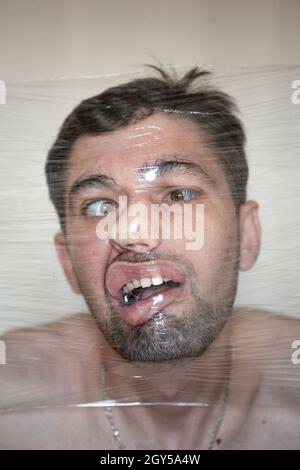 Das Gesicht eines Mannes in einer Plastikfolie. Fleischbehälter Stockfoto