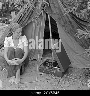 Werbefoto für das Klepper Zelt: getreu dem Werbeslogan „wahre fröhlich in die weite Welt, mit Klepper-Mantel, -Boot und -Zelt“ sitzt eine junge Frau mit einem Grammophon vor einem Zelt, Deutschland 1930er Jahre. Werbung für ein Klepper-Zelt: Eine junge Frau, die mit einem Grammophon vor einem Zelt sitzt, Deutschland 1930er Jahre. Stockfoto