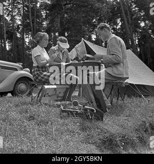 Ein Mann und zwei Frauen Artikel eine Einems Klapptisch vor einem Zelt, Deutschland 1930er Jahre. Ein Mann und zwei Frauen an einem Tisch sitzen vor einem Zelt, Deutschland 1930. Stockfoto