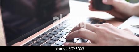 Weibliche Hände, die auf der Laptop-Tastatur tippen, halten Glas mit Kaffee Stockfoto