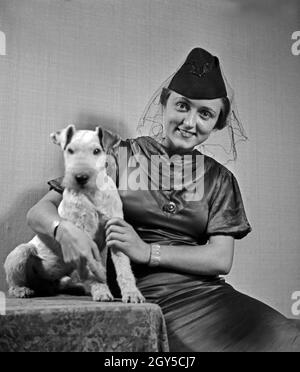 Eine Dame mit Hund im Fotostudio in zeitgenössischer Mode, Deutschland 1930er Jahre. Eine Frau und ihr Hund Haustier auf dem Foto Studio in der zeitgenössischen Mode, Deutschland 1930. Stockfoto