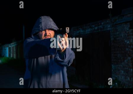 Kaukasischer Mann in einer Kapuze schießt eine Pistole. Stockfoto
