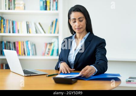 Seriöse hispanische reife Geschäftsfrau, die am Schreibtisch im Büro mit Dokumenten arbeitet Stockfoto