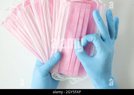 Arzt in blauen Einweghandschuhen hält viele medizinische Masken und Geste ist ausgezeichnet Stockfoto