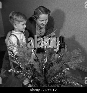 Ein kleiner Junge schreibt-Wunschzettel an den Weihnachtsmann mit der Schreibmaschine und gibt ihn seiner Mutter zur Weiterleitung, Deutschland 1930er Jahre. Ein kleiner Junge mit der Eingabe seiner Liste der Wünsche und gibt ihm seine Mutter zur Weiterleitung an Santa, Deutschland 1930. Stockfoto