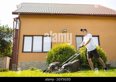 Mann mäht das Gras mit einem Benzinrasenmäher im Hinterhof des Hauses Stockfoto
