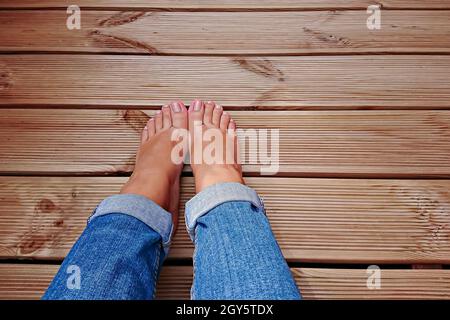 POV-Ansicht der Barfußbeine der Frau in blauer Jeans auf Holzboden mit Platz für Kopien Stockfoto