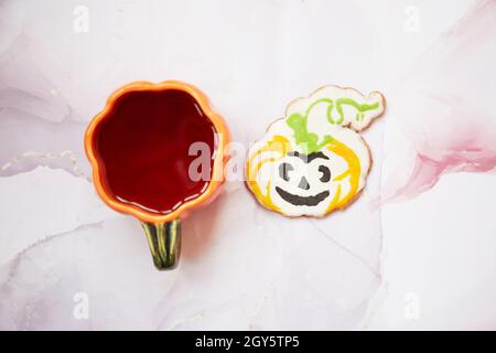 Halloween Kreativkonzept: Kürbisbecher und selbstgemachter Keks in Form von niedlichem Kürbis-Nahaufnahme. Ästhetische Herbststimmung oder Trick or Treat Konzept. Herbst Stockfoto