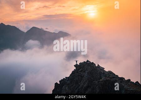 Der Mensch steht allein auf dem Gipfel des Felsens. Wanderer beobachten die Herbstsonne am Horizont. Schöner Moment das Wunder der Natur. Bunter Nebel im Tal. Mann h Stockfoto