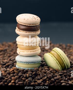 Stapel von mehrfarbigen Macarons liegt auf gerösteten Kaffeebohnen, schwarzem Hintergrund, köstlichen und exquisiten Dessert Stockfoto