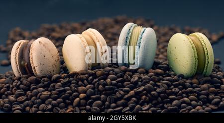 Mehrfarbige Macarons liegen auf gerösteten Kaffeebohnen, schwarzer Hintergrund, köstliches und exquisites Dessert, Nahaufnahme Stockfoto