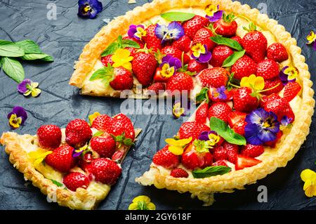 Erdbeerkuchen in Scheiben, verziert mit essbaren Blumen und Minze.Trendy Summer Berry Pie Stockfoto