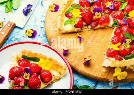 Erdbeerkuchen in Scheiben, verziert mit essbaren Blumen und Minze.Trendy Summer Berry Pie Stockfoto