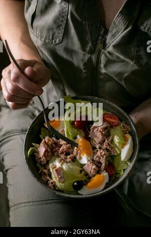 Frau hält in einer Schüssel mit Nicoise-Salat mit Thunfischkonserven, Oliven und Eiern. Omega 3 vegetarisches Gericht Stockfoto