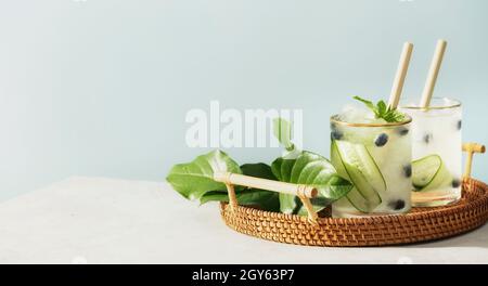 Trendiges und gesundes Sommervitaminwasser mit Gurke, Minze und Heidelbeere in Weidenschale auf blauem Himmel Hintergrund, Banner Stockfoto