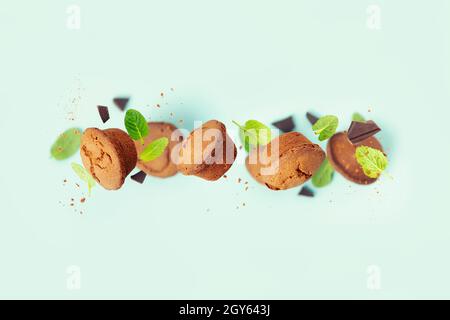 Schokoladen-Muffins mit Minzblättern und Schokoladenstücken auf blauem Hintergrund Stockfoto