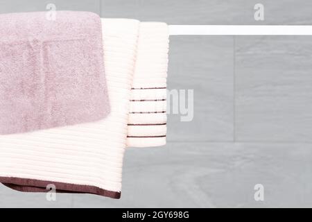 Handtücher zum Aufhängen. Nahaufnahme von violetten und beigefarbenen weichen Frottee-Badetüchern hängen an einer Kleiderstange vor einem abstrakten, unscharfen, hellen Hintergrund. Stockfoto