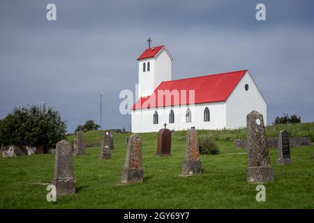 Hafnarfjordur, Island - 17. Juli 2021: Traditionelle isländische Kirche mit rotem Dach, alte vertikale Grabsteine auf dem Friedhof vor der Kirche Stockfoto