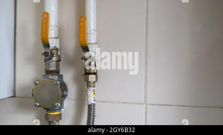Gelbe Ventile und Erdgasleitungen in einem modernen Heizraum in einer Küche mit Keramikfliesen. Gasventil Kugelhahn, Gas-und Sanitär-Ausrüstung Stockfoto