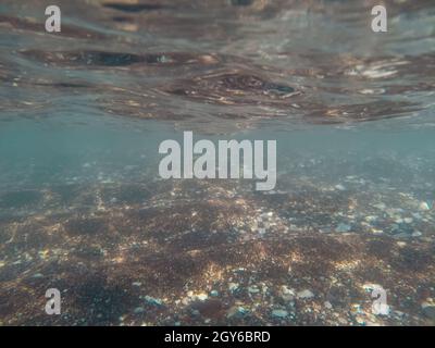 Sonnenlicht unter Wasser auf einem flachen Kiesboden im Mittelmeer. Verschwommene Unterwasserfotografie. Stockfoto