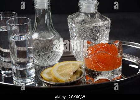 Roter Kaviar in Schale auf silbernem Tablett auf schwarzem Hintergrund mit Wodka Stockfoto