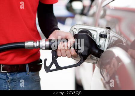 Tankstellenmitarbeiter in roter Uniform füllen Bronze Pickup LKW-Tank. Nahaufnahme Hand mit schwarzer Gaspumpendüse. Stockfoto