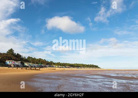 Reihe von Strandhütten mit Blick auf Holkham Bay in Wells-Next-the-Sea an der Nord-Norfolk-Küste an einem hellen und sonnigen Oktobermorgen mit Menschen zu Fuß Stockfoto