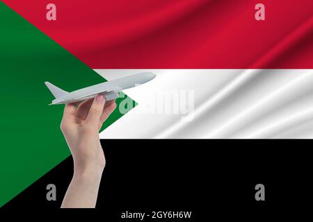 Flugzeug in der Hand mit der Nationalflagge des Sudan. Reise nach Sudan. Stockfoto