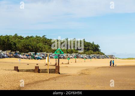 Reihe von Strandhütten mit Blick auf Holkham Bay in Wells-Next-the-Sea an der Nord-Norfolk-Küste an einem hellen und sonnigen Oktobermorgen mit Menschen zu Fuß Stockfoto