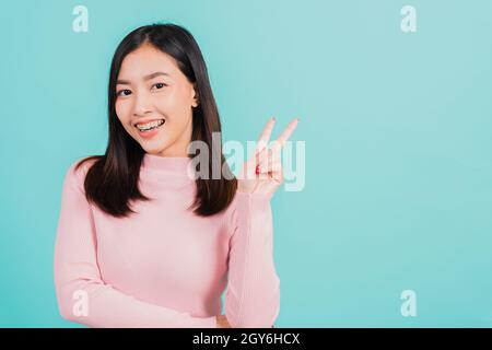 Junge asiatische schöne Frau lächelnd tragen Silikon kieferorthopädische Halter auf den Zähnen zeigt V-Zeichen Sieg Finger isoliert auf blauem Hintergrund, Beibehaltung Stockfoto