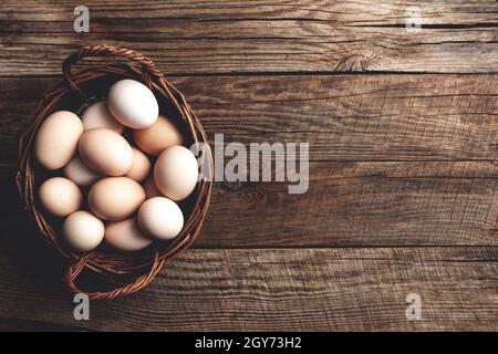 Flach legen mit Korb voller Bio-Hühnereier auf Holz Hintergrund. Bio-Haushaltskonzept mit Eiern von Freiland- und Weidegehennen Stockfoto