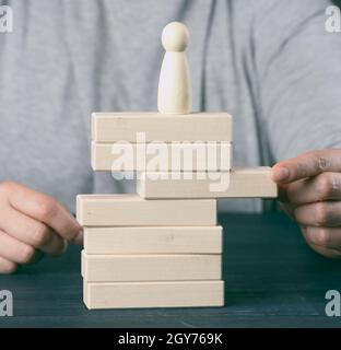 Die Hand der Frau zieht einen Holzblock aus dem Turm, auf dem die Figur steht. Das Konzept der Reputationsrisiken, Hindernisse in der Wirtschaft, unfavorab Stockfoto