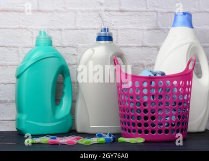 Rosafarbener Wäschekorb und Plastikflaschen mit flüssigem Reinigungsmittel auf weißem Backsteinwand-Hintergrund Stockfoto
