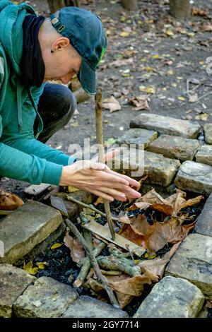 Mann, der ein Feuer für den Grill im Wald mit einer Technik der Reibung. Mit primitiven Werkzeugen überleben Handwerk und Fähigkeiten üben. Stockfoto