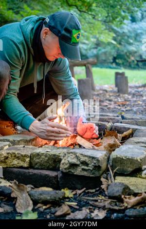 Mann, der ein Feuer für den Grill im Wald mit einer Technik der Reibung. Mit primitiven Werkzeugen überleben Handwerk und Fähigkeiten üben. Stockfoto